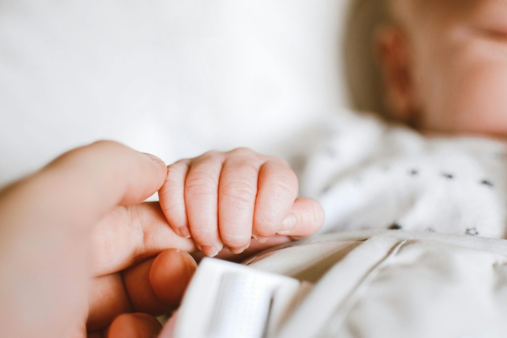 Noworodek trzyma palec mamy, której doskwierają powikłania po porodzie.